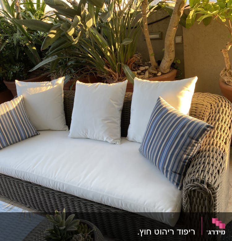 כריות לבנות וכחולות על ספה קלועה בגינה